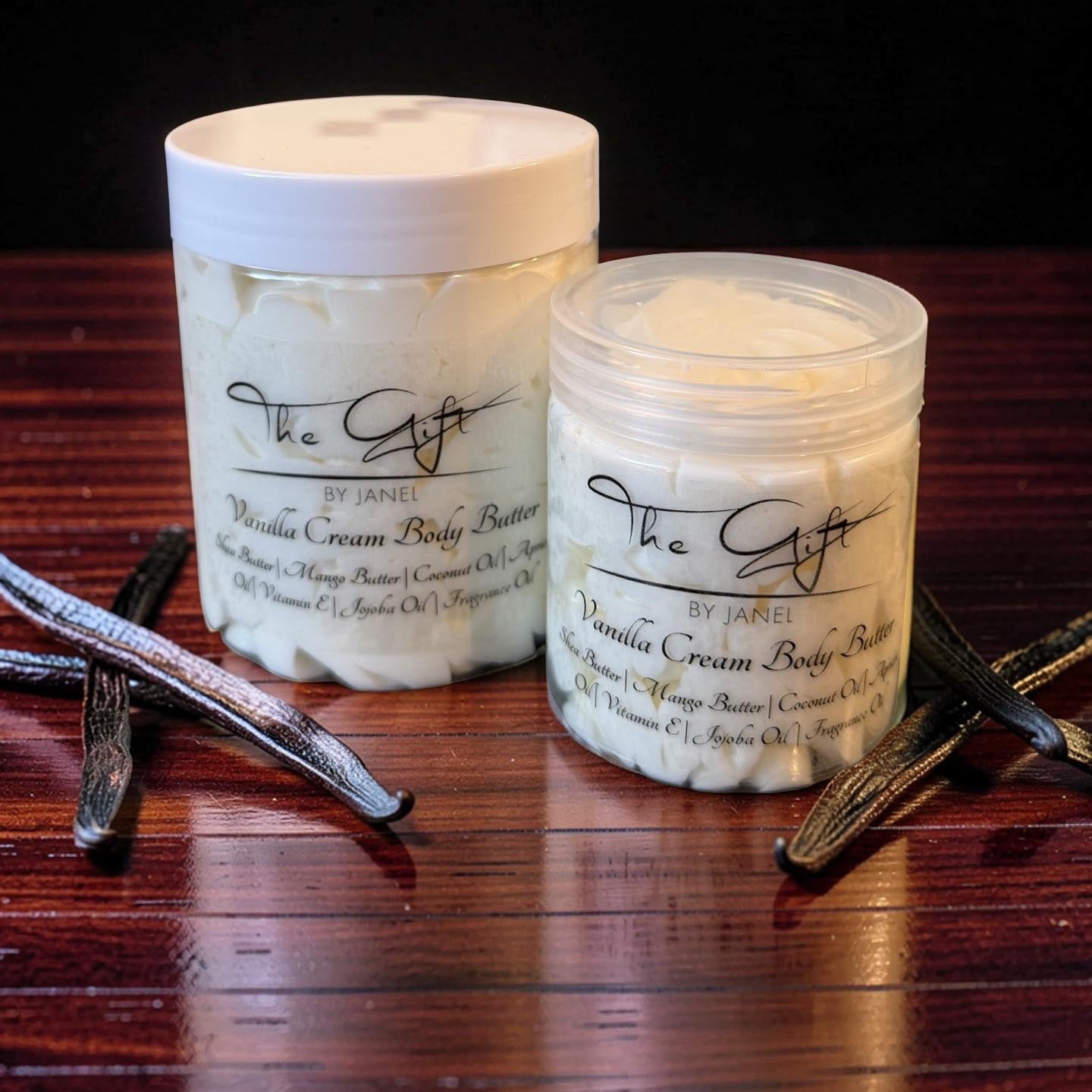 Two containers of Vanilla Cream Body Butter on a wooden surface with vanilla beans.