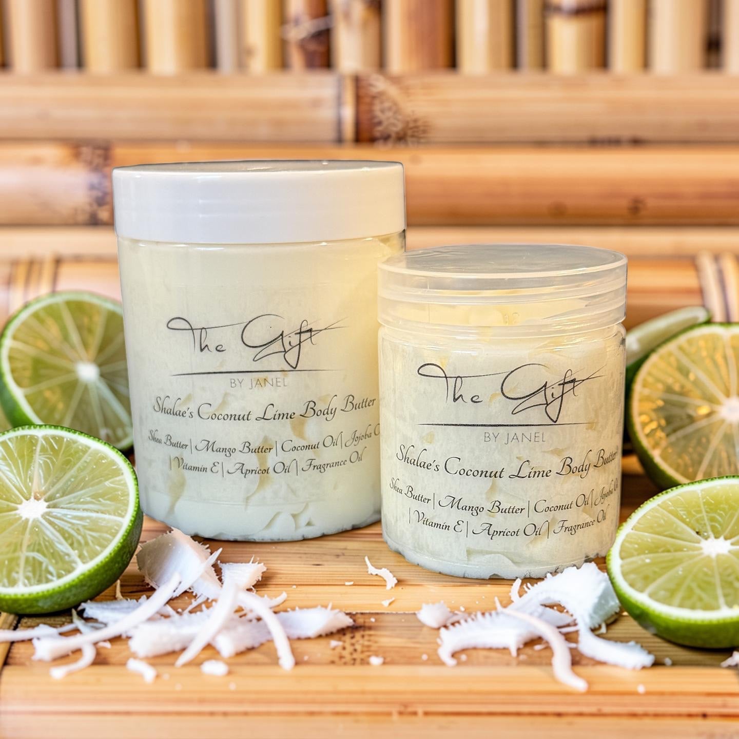 Two jars of 'The Gift by Janel natural coconut lime body butter set on a wooden board, surrounded by lime slices, coconut flakes, and shredded coconut against a neutral background.