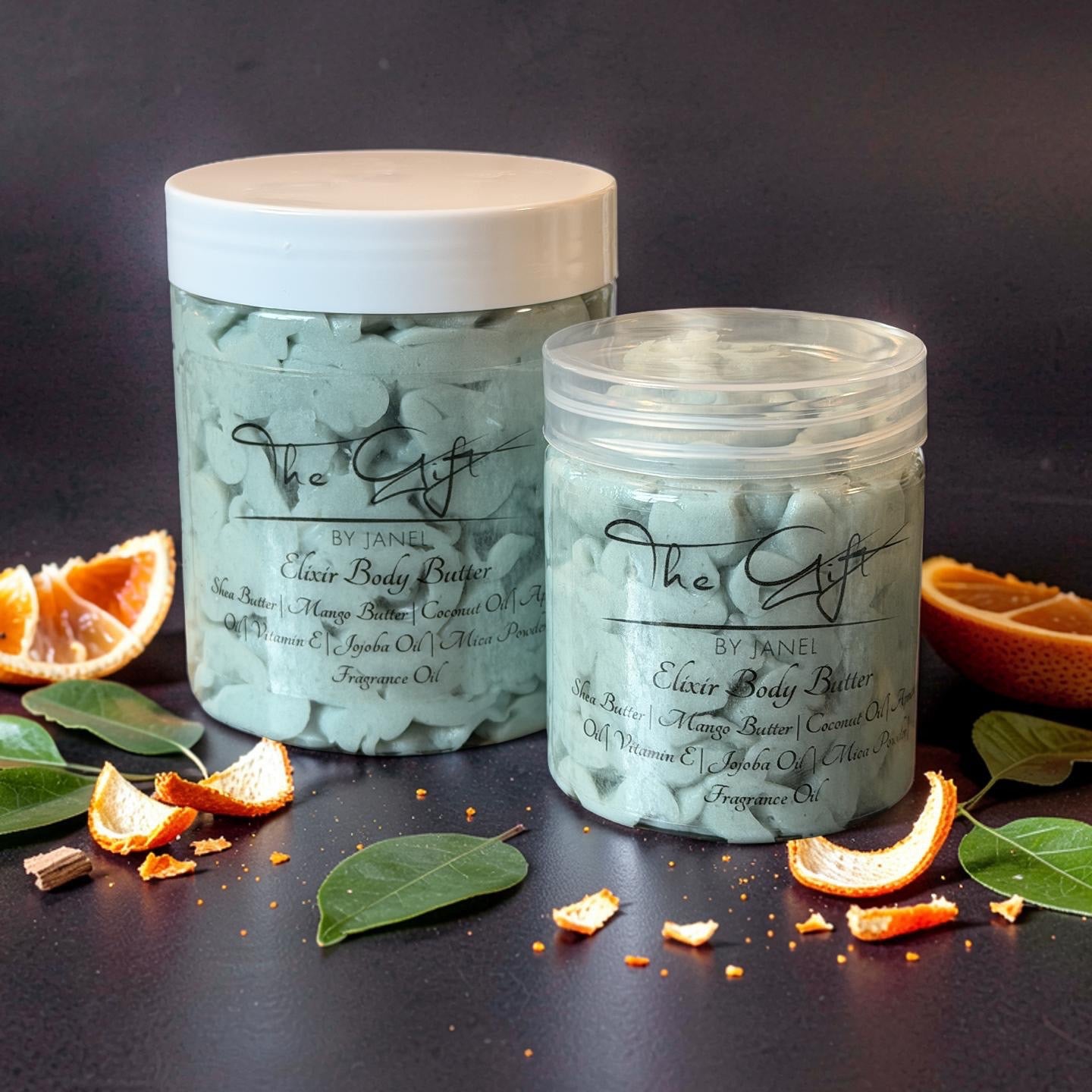 Two jars of 'The Gift' body scrub with orange slices and leaves on a dark background