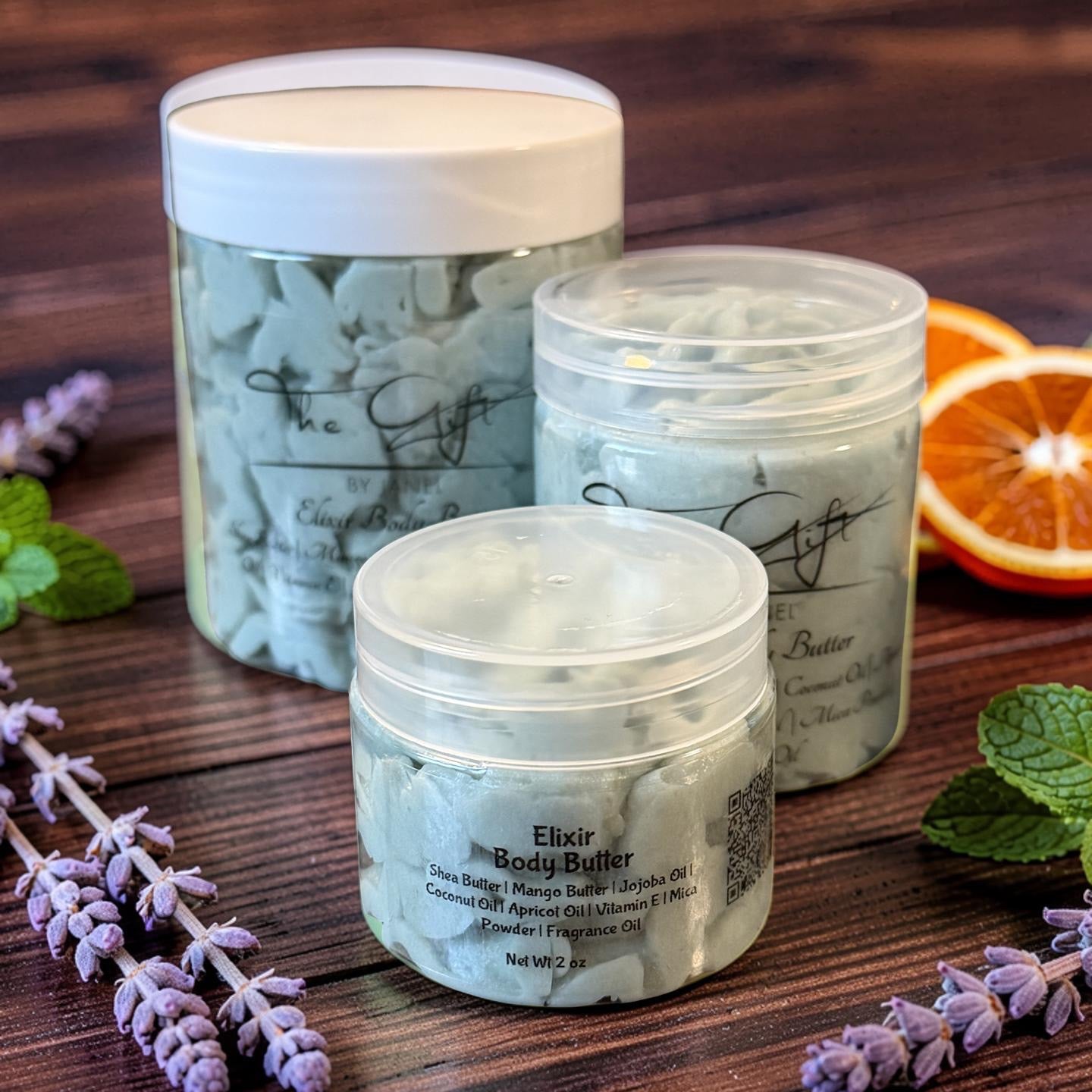 Three containers of body butter on a wooden surface with lavender and orange slices.