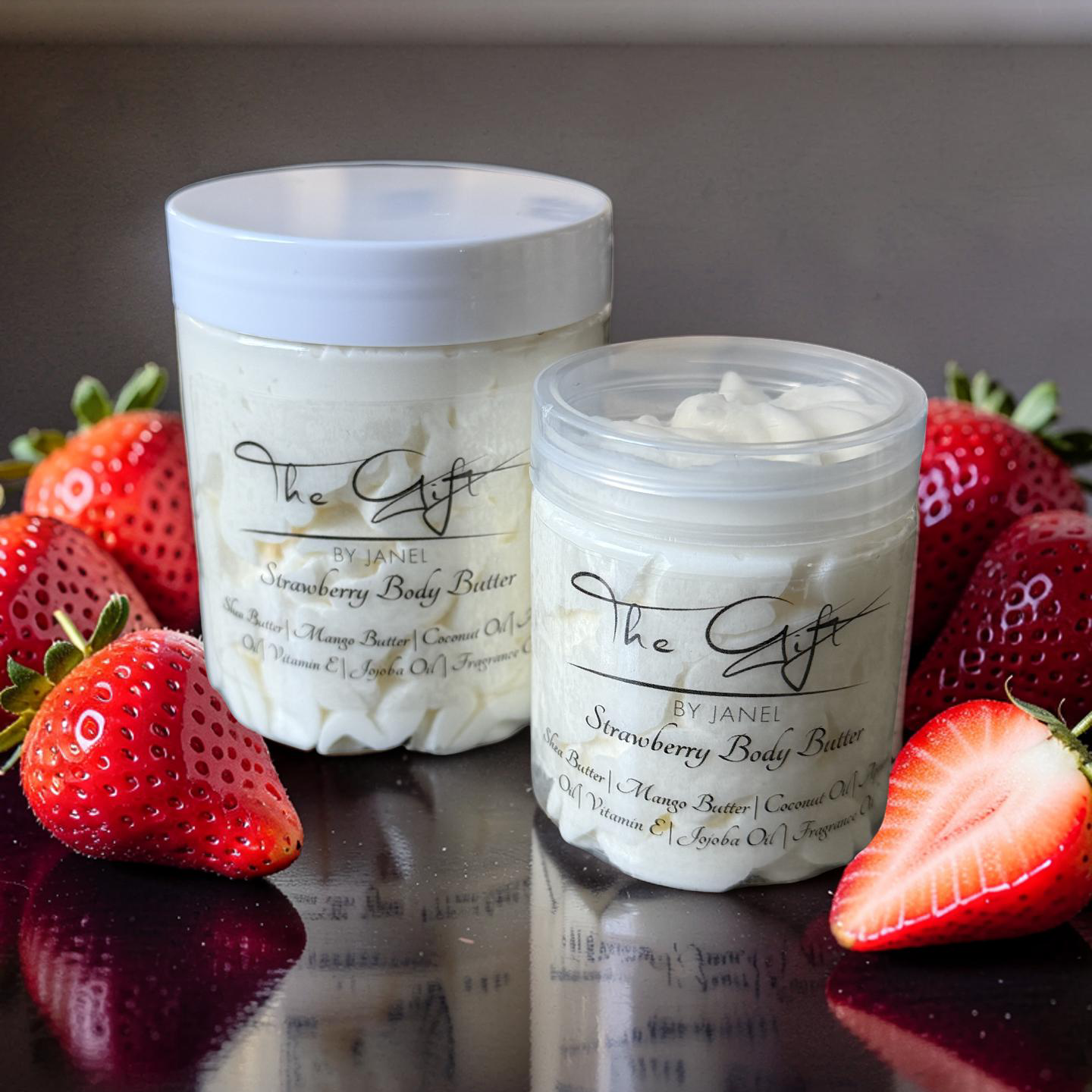 Two containers of strawberry body butter with strawberries on a reflective surface