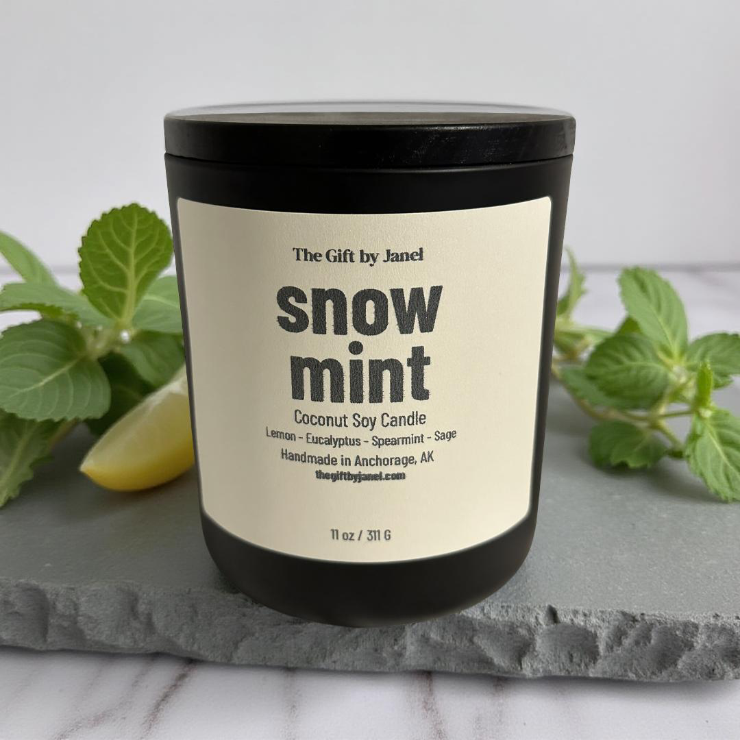 Snow mint candle with label on a gray surface with green leaves in the background
