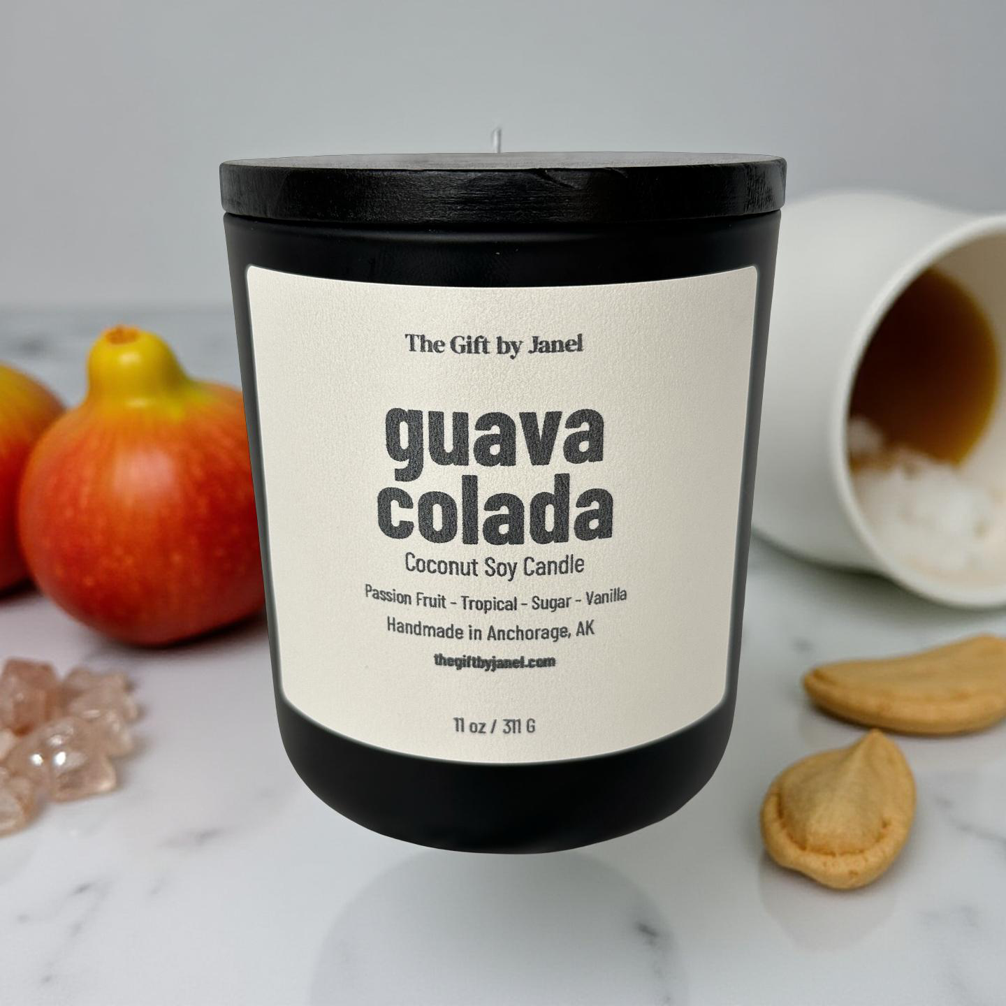 Candle labeled 'guava colada' with apples and cookies on a marble surface