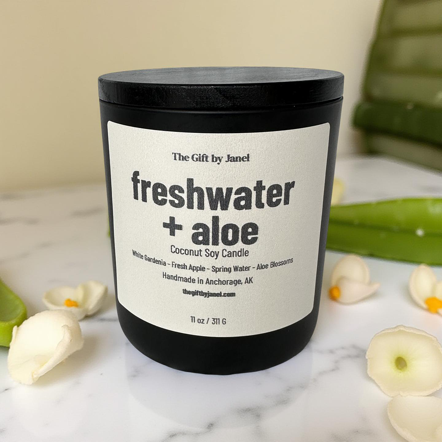 Candle labeled 'freshwater + aloe' on a marble surface with aloe and gardenia.