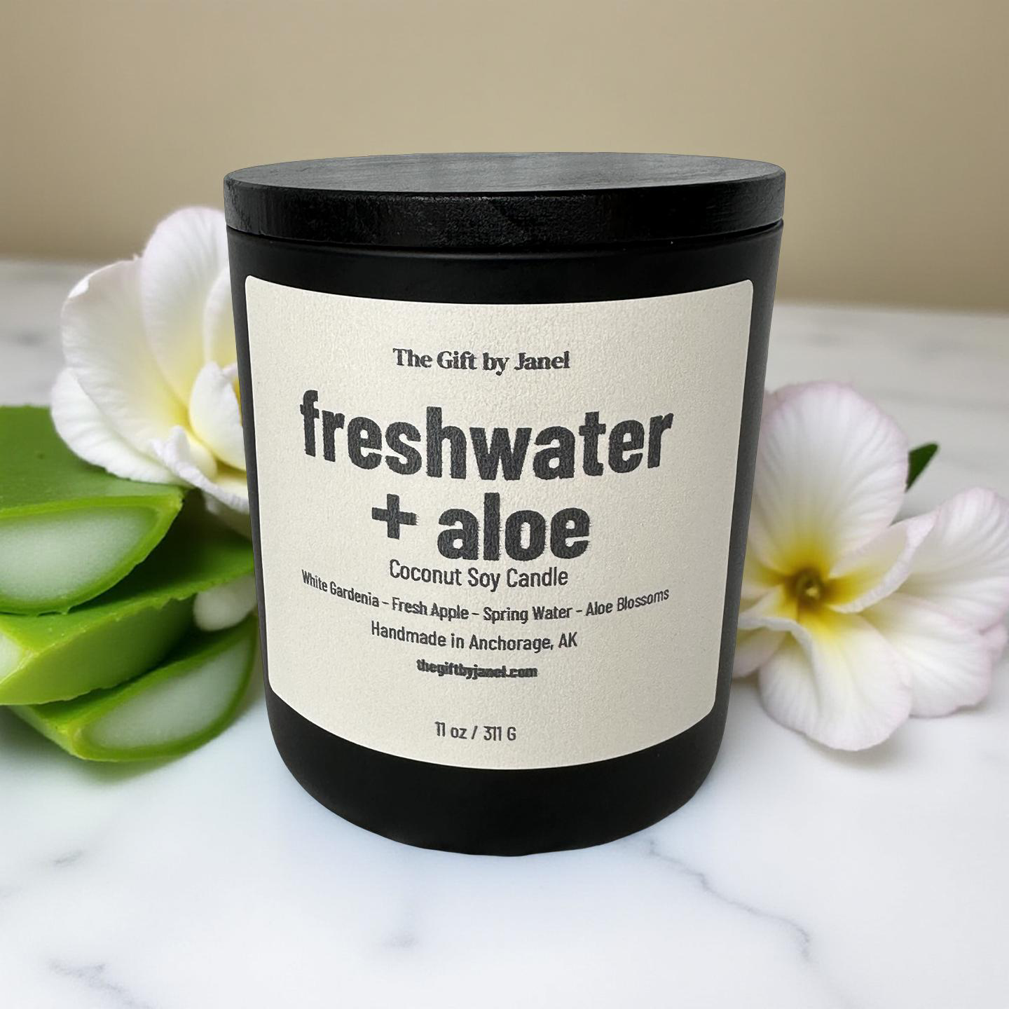 Candle labeled 'freshwater + aloe' on a marble surface with aloe and gardenia.
