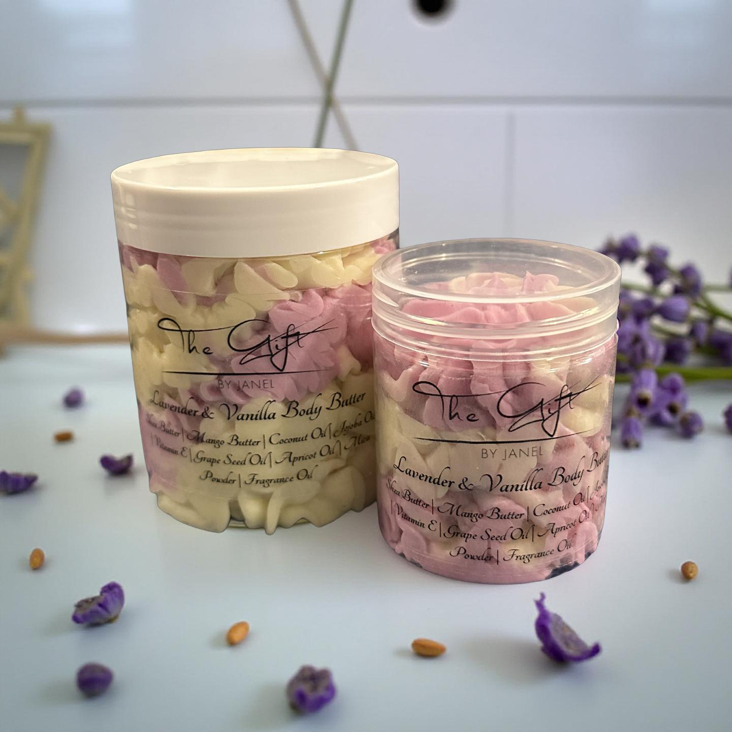 Two containers of lavender and vanilla body butter with flowers on a white surface.