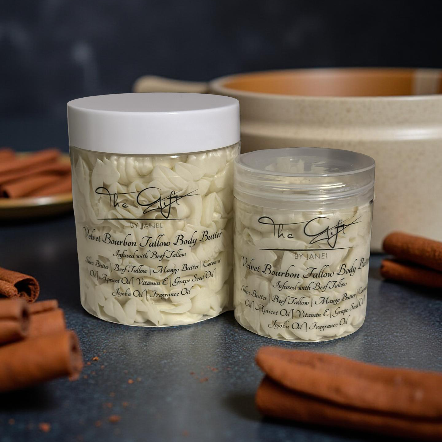 Two containers of body butter with cinnamon sticks on a dark surface