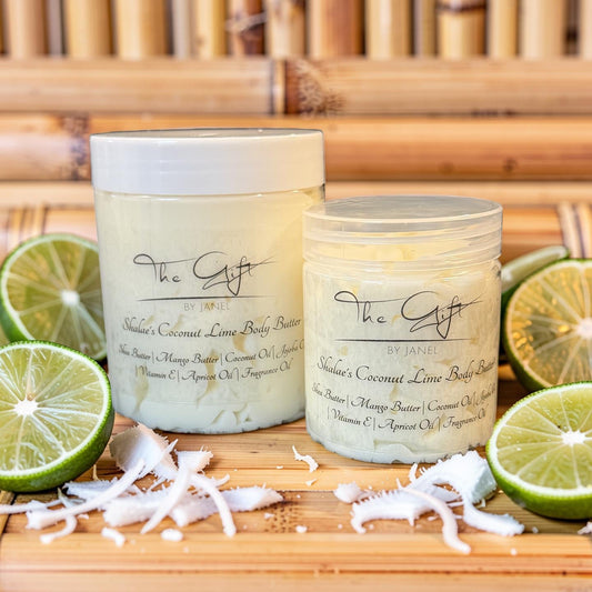 Two jars of 'The Gift by Janel natural coconut lime body butter set on a wooden board, surrounded by lime slices, coconut flakes, and shredded coconut against a neutral background.