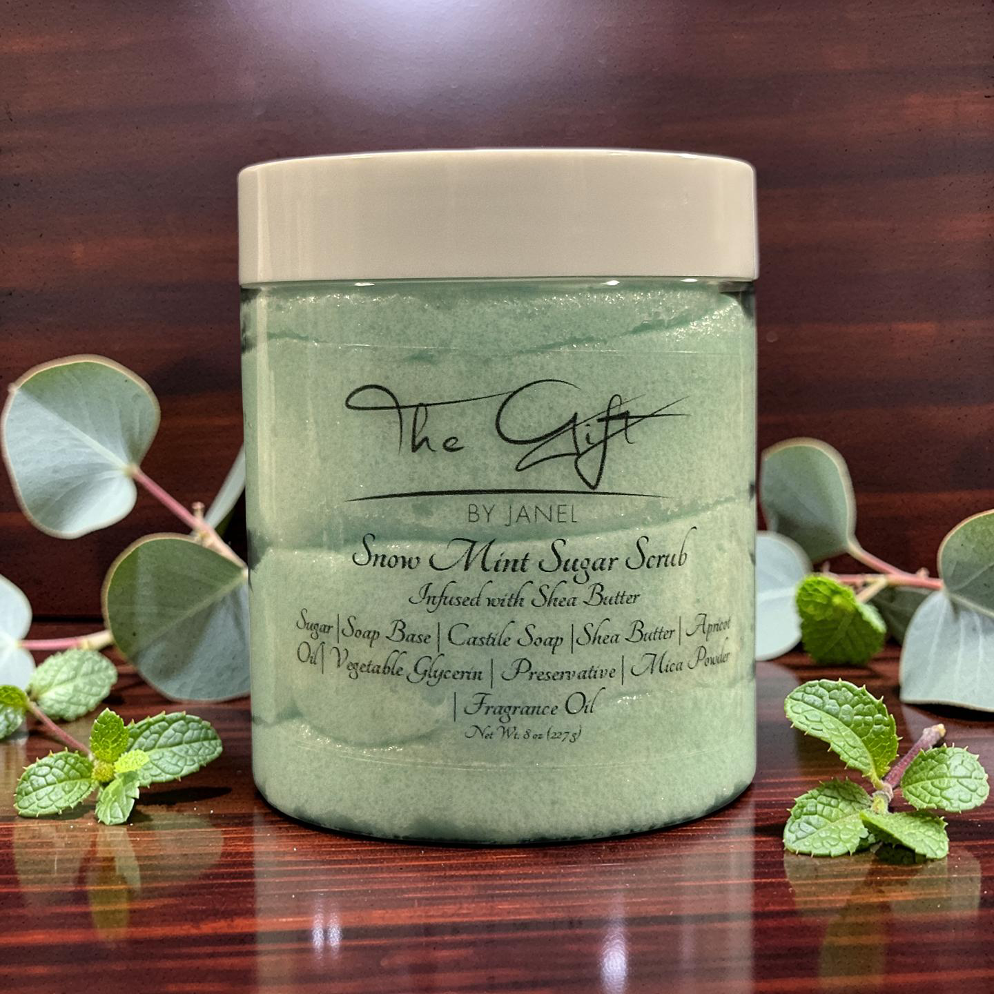 Jar of Snow Mint Sugar Scrub with mint leaves on a wooden surface