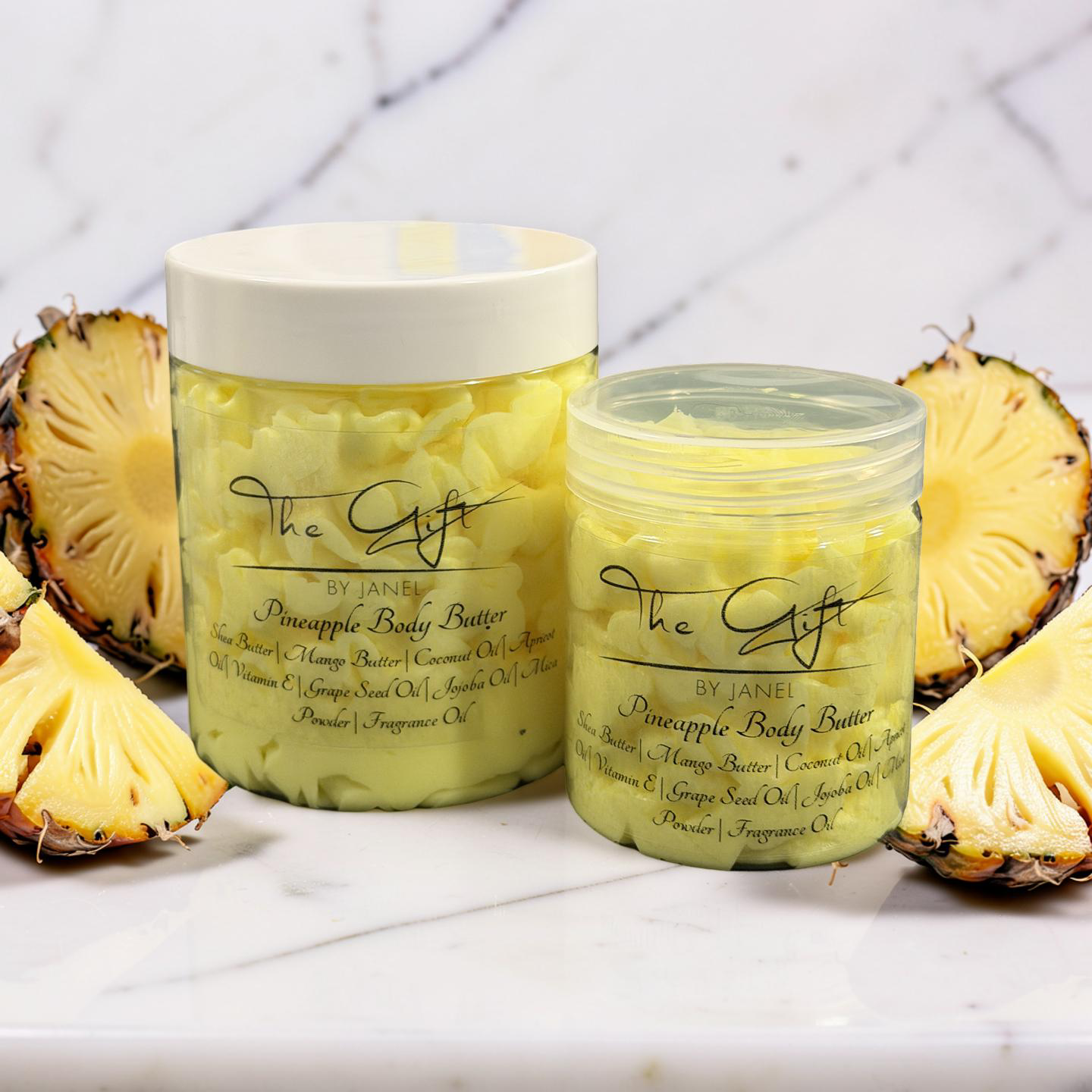 Two jars of pineapple body butter with pineapple slices on a white surface.