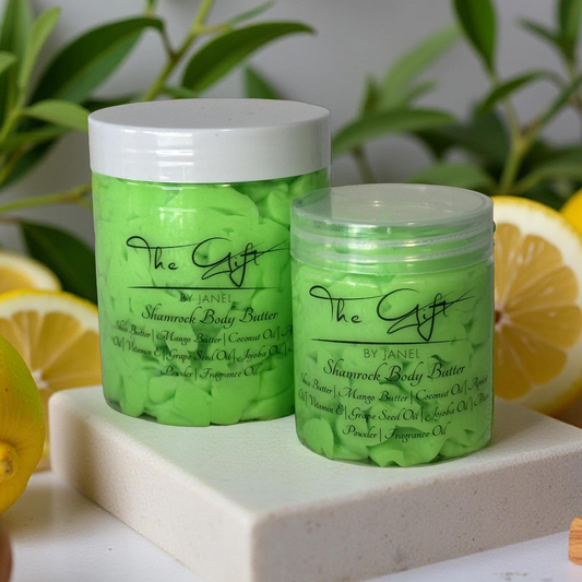 Two green jars of The Gift by Janel Shamrock Body Butter on a white surface with lemons and green leaves in the background.