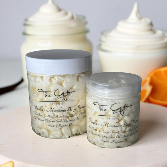 Two jars of The Gift by Janel body butter on a white plate with orange slices in the background.